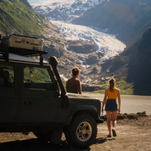 Bianca, Tim and their Land Rover Defender stand in front of a big glacier that sits between two massive mountains in the background.