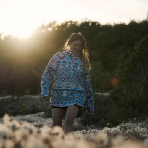 Brand shoot cosy fleece hoodie: Bianca stands in a field of white fluffy flowers. The sun is setting in the background.