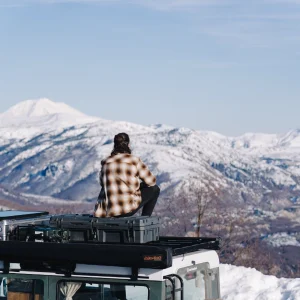 Its winter. Tim sits on the roof of their Land Rover Defender, starring in the distance towards Mount St. Helens in Washington.