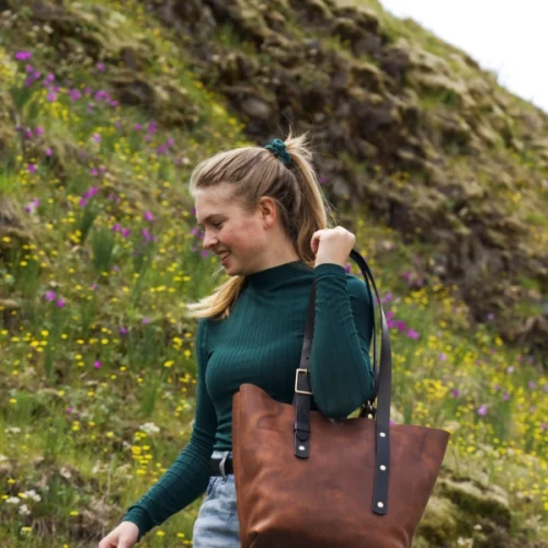 Brand shoot leather goods: Bianca in a flower field. She carries a brown leather bag over her shoulder. She looks like she is about to sit down for a picnic.